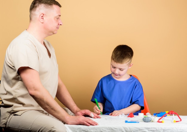 Bambino felice con il padre con lo stetoscopio. padre e figlio in uniforme medica. medico di famiglia. fiducia e valori. bambino con papà in ospedale. medicina e salute. bambino felice gioca con papà.