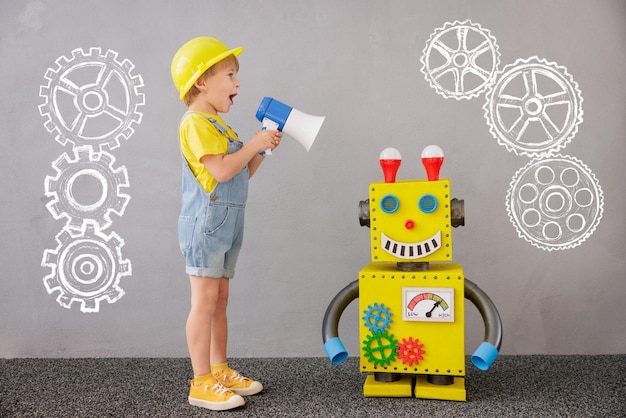 Bambino felice con il robot. Bambino divertente che gioca a casa. Ragazzo che grida sopra l'altoparlante. Concetto di tecnologia di successo, creatività e innovazione