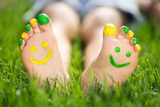 Bambino felice con il sorriso sui piedi all'aperto Bambino sdraiato sull'erba verde primaverile Concetto di ecologia e stile di vita sano