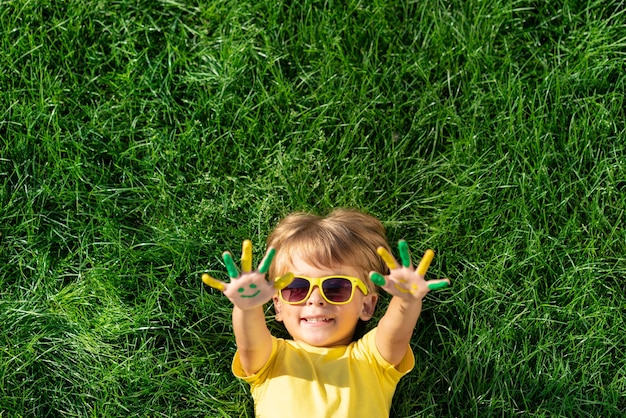 Bambino felice con il sorriso sulle mani all'aperto. Capretto sull'erba verde della sorgente. Concetto di ecologia e stile di vita sano