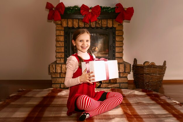 Bambino felice con la confezione regalo sullo sfondo del camino di Natale