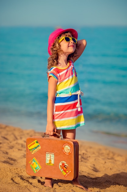 Bambino felice con la valigia vintage sulla spiaggia