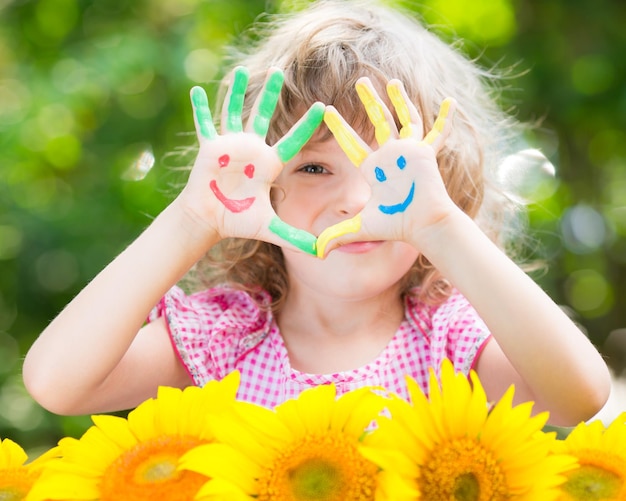 Bambino felice con lo smiley sulle mani su sfondo verde primavera