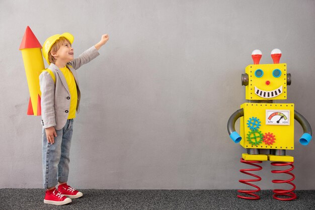 Bambino felice con razzo e robot. Bambino divertente che gioca a casa. Concetto di tecnologia di successo, creatività e innovazione