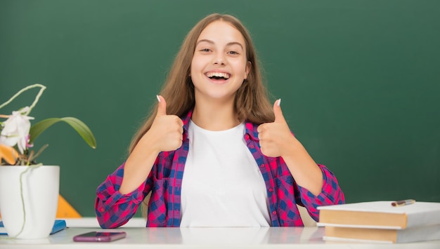 Bambino felice dell'infanzia pronto a studiare il pollice in su ragazza adolescente torna a scuola concetto di istruzione giorno della conoscenza bambino in classe su sfondo lavagna 1 settembre