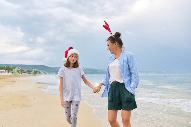 Bambino felice della figlia e della mamma in cappello della Santa che cammina tenendosi per mano lungo la spiaggia