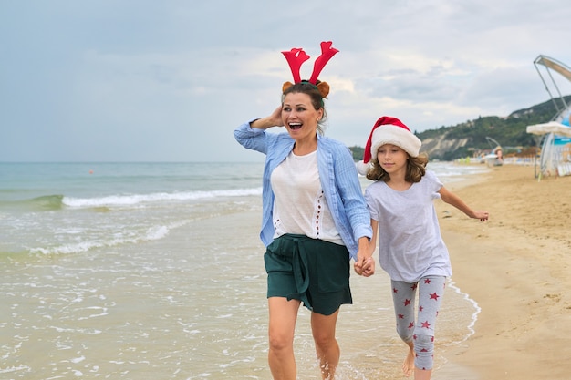 Bambino felice della figlia e della mamma in cappello della Santa che cammina tenendosi per mano lungo la spiaggia