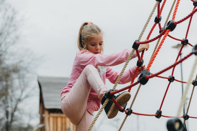 Bambino felice della ragazza dell'adolescente che gioca nella ragnatela della corda al campo da giuoco. sport per bambini.