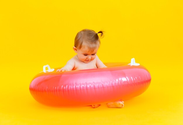 Bambino felice di 10 mesi con un cerchio di nuoto seduto su uno sfondo giallo, foto in studio del bambino in un cerchio di nuoto