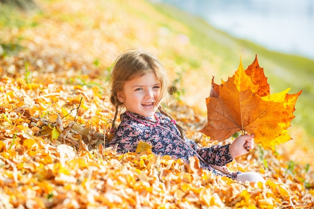 Bambino felice di autunno divertendosi con le foglie all'aperto nel parco. Foglie che cadono sfondo naturale.