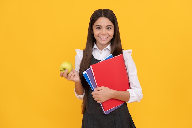 Bambino felice di nuovo a scuola che tiene mela e libri formazione di sfondo giallo