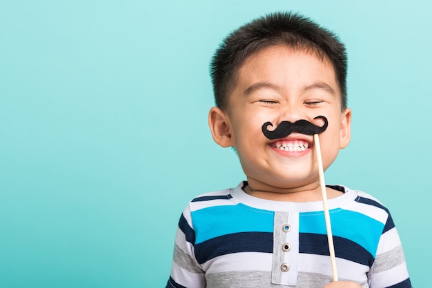 Bambino felice divertente che tiene i puntelli dei baffi neri per il fronte vicino della cabina fotografica