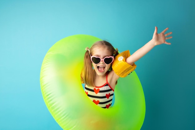 Bambino felice divertente in costume da bagno luminoso e occhiali da sole sorridente e in possesso di un anello di nuoto