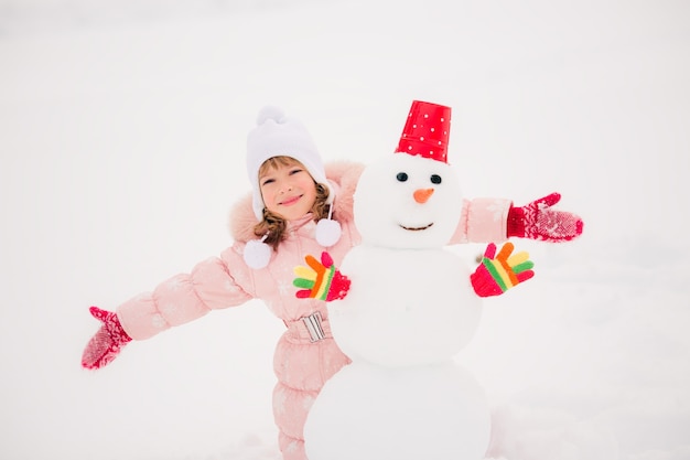 Bambino felice e pupazzo di neve nel parco invernale