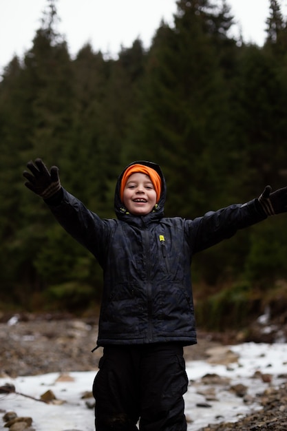 Bambino felice in abiti sportivi cammina attraverso un fiume di montagna ghiacciato
