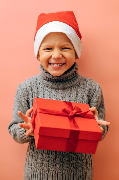 Bambino felice in cappello di Babbo Natale con confezione regalo su sfondo rosso Celebrazione di Natale