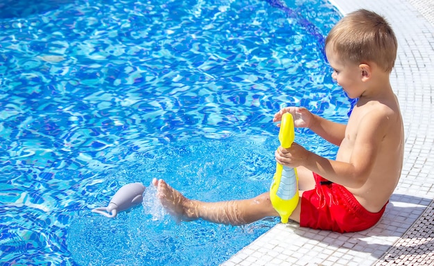 Bambino felice in piscina che gioca con una pistola ad acqua.