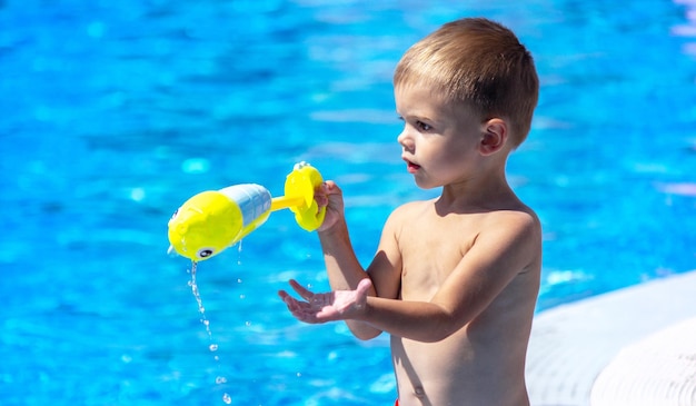 Bambino felice in piscina che gioca con una pistola ad acqua.