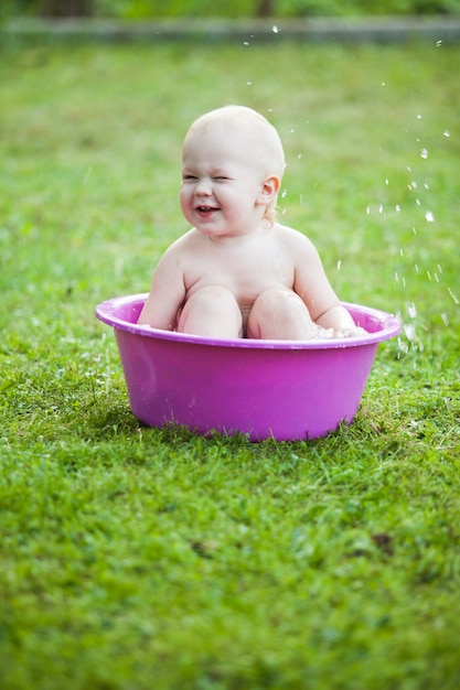 Bambino felice in una bacinella sull'erba in cortile