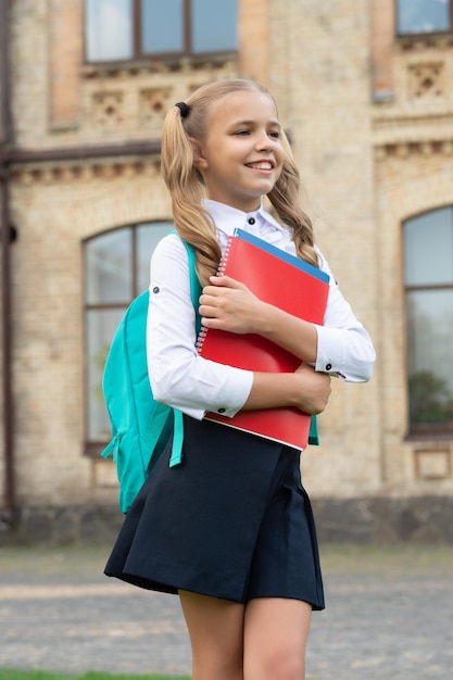 Bambino felice in uniforme che torna a scuola portando libri e istruzione zaino