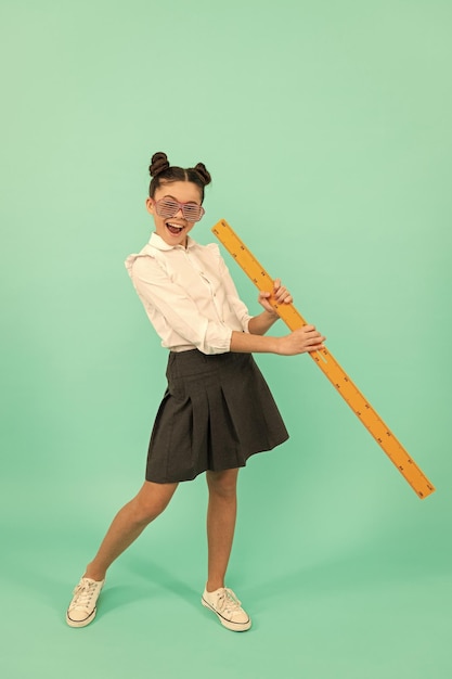 Bambino felice in uniforme scolastica e occhiali con righello matematico su sfondo blu infanzia