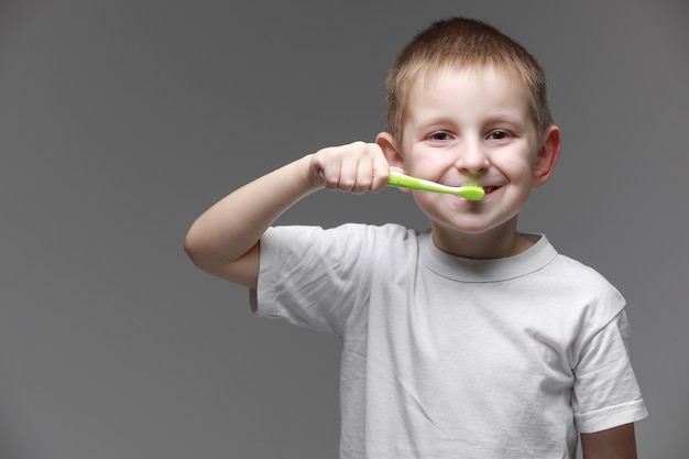 Bambino felice kid boy lavarsi i denti con spazzolino da denti su sfondo grigio. Assistenza sanitaria, igiene dentale. Mockup, copia spazio.