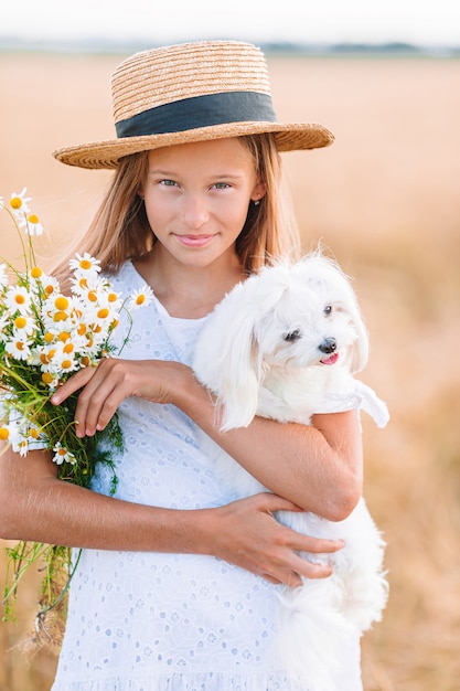 Bambino felice nel campo di grano. Bella ragazza in abito bianco in un cappello di paglia con grano maturo nelle mani