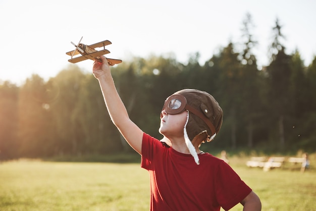 Bambino felice nel casco pilota giocando con un aeroplanino giocattolo di legno e sognando di diventare volante