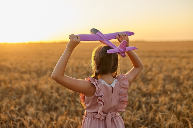 Bambino felice, ragazza che gioca con l'aeroplano giocattolo sul campo di grano estivo. La piccola figlia sogna di volare. Bambino spensierato che gioca all'aperto