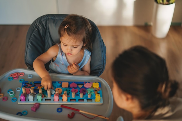 Bambino felice seduto sul seggiolone e giocando con i giocattoli di legno in una casa moderna e luminosa Bambino carino che gioca con i giocattoli