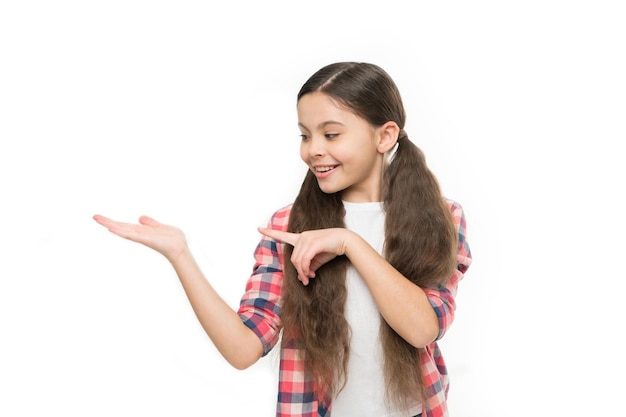 Bambino felice sorridente volto allegro con adorabile acconciatura mostra qualcosa sul palmo aperto copia spazio Concetto di capelli forti Kid capelli lunghi sani e lucenti Bambina crescere capelli lunghi Abitudini di cura dei capelli sane