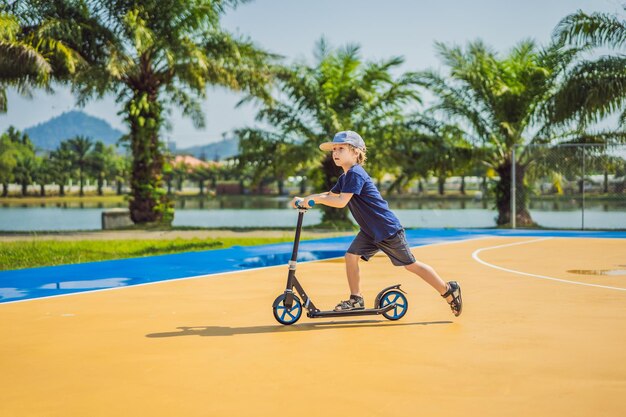 Bambino felice sul motorino di calcio sul campo da basket i bambini imparano a pattinare sulla tavola a rotelle ragazzino