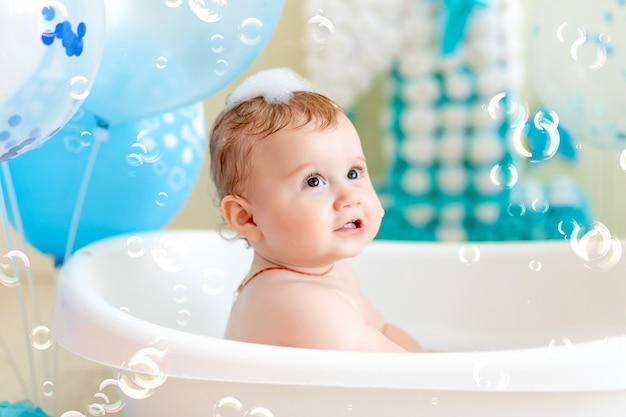 bambino festeggia il compleanno 1 anno in una vasca da bagno con palloncini, bagnando il bambino con palloncini blu