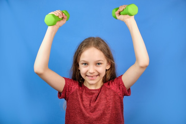 Bambino fitness. Ritratto di una ragazza sportiva con manubri su uno spazio blu