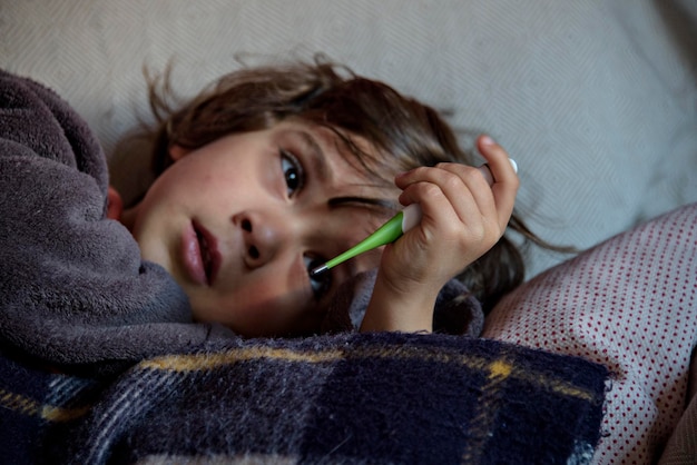 Bambino freddo sdraiato sul letto guardando il termometro