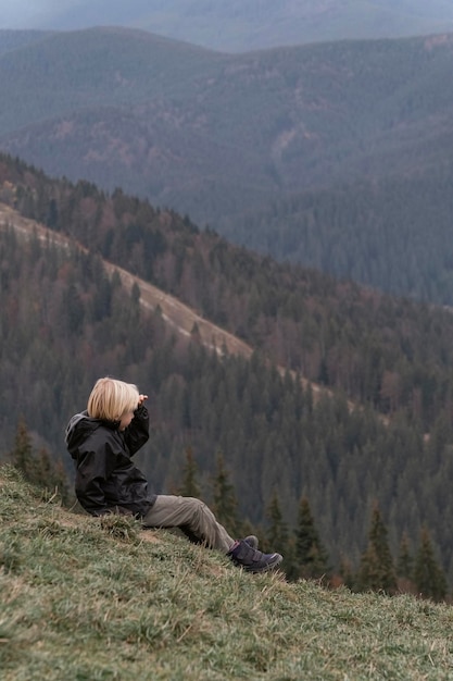 Bambino guarda la distanza in vacanza in montagna Scolaro biondo si siede in collina Cornice verticale