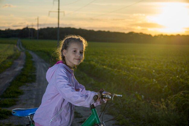 Bambino in bicicletta su uno sfondo di campo verde e con i raggi del sole della sera