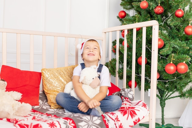 Bambino in cappello della Santa vicino all'albero di Natale