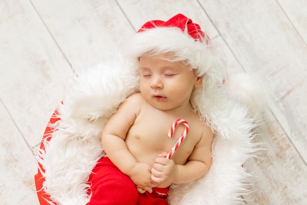 Bambino in costume da Babbo Natale che dorme su uno sfondo di legno chiaro