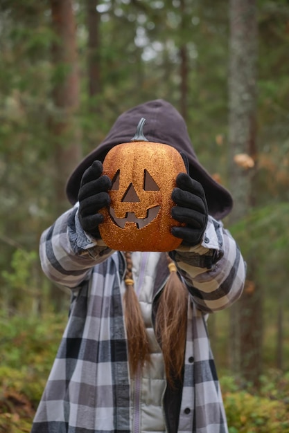 Bambino in costume di halloween che tiene una zucca lanterna decorativa davanti al suo viso