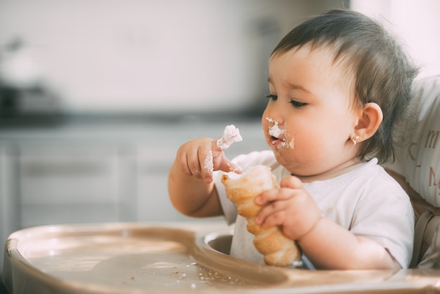 Bambino in cucina che mangia avidamente le deliziose corna alla crema, ripiene di crema alla vaniglia