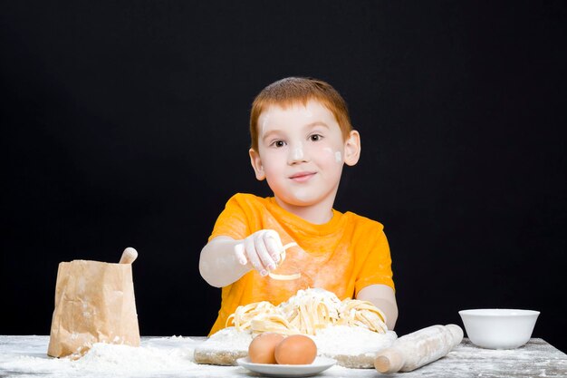 Bambino in cucina mentre aiuta a preparare il cibo ragazzo con i capelli rossi e belle caratteristiche facciali bambino che gioca con la farina in cucina