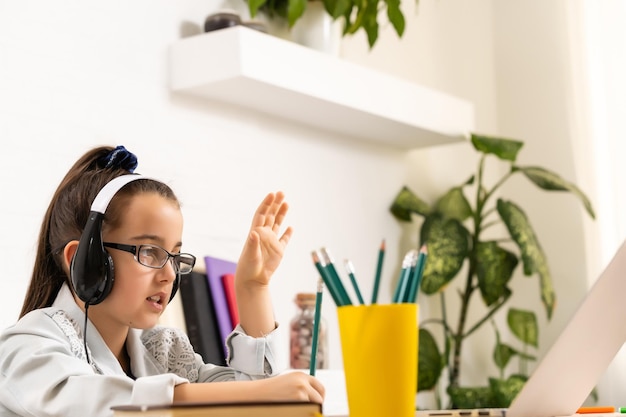 Bambino in linea. Una bambina usa una chat video portatile per comunicare l'apprendimento mentre è seduta a un tavolo a casa.