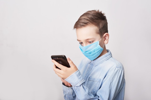 Bambino in maschera medica con telefono cellulare. Coronavirus e concetto di inquinamento atmosferico pm2.5. Sintomi del virus. Concetto di epidemia, influenza, protezione dalle malattie, vaccinazione. Malattia influenzale. Cure mediche.