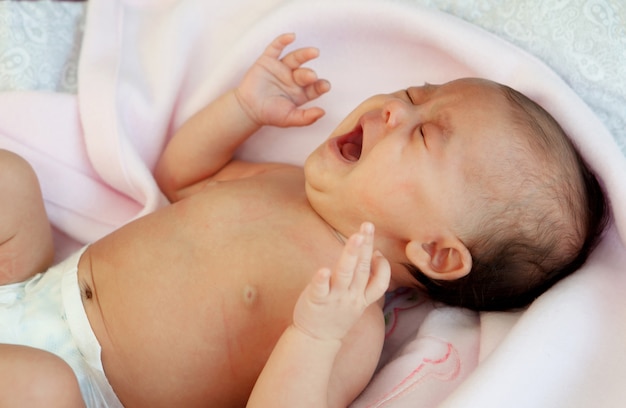 Bambino in pannolino avvolto in una coperta rosa piangendo