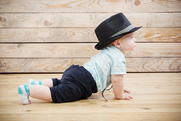 Bambino in pantaloncini cappello nero, camicia e bretelle su una superficie di legno