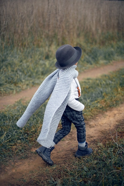 Bambino in pantaloni a quadri, cappello, bretelle e sciarpa in piedi in un campo