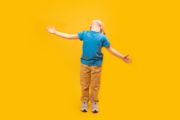 Bambino in piedi su sfondo giallo che indossa una maglietta blu e alzò le mani La ragazza guarda in alto