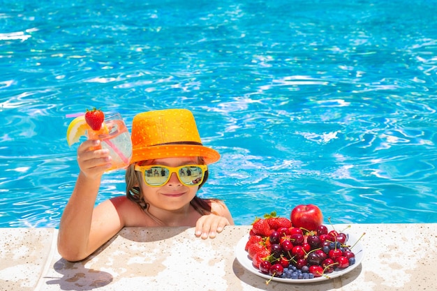 Bambino in piscina che mangia frutta e beve un cocktail di limonata Concetto di vacanza estiva per bambini