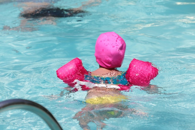 Bambino in piscina con galleggiante rosa con acqua blu